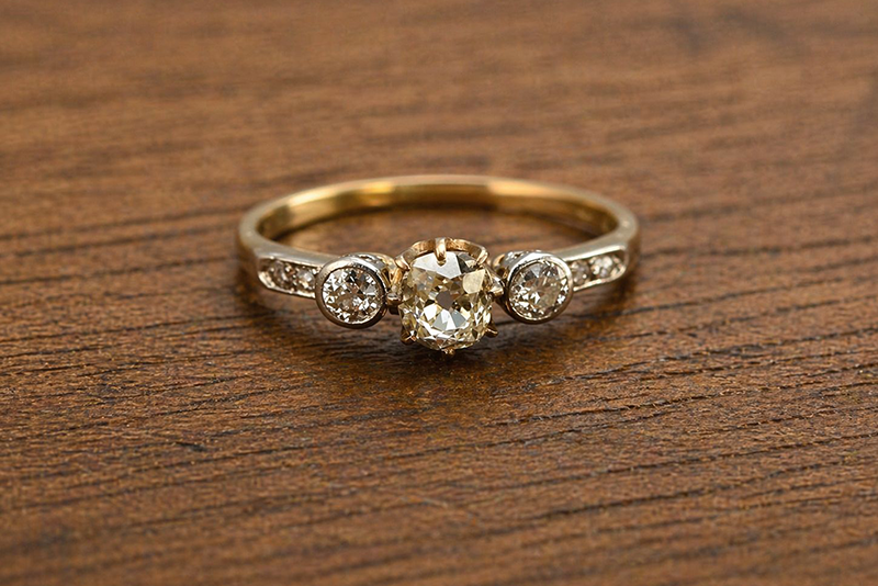 An antique diamond ring set with Old European Cut diamonds rests on a wooden surface