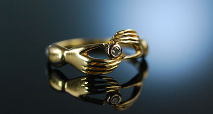 Goldener Ring mit dem Motiv zweier Hände und mittigem Diamant