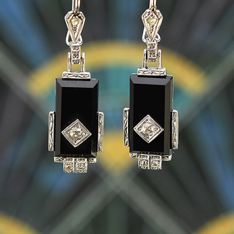 Ein Paar Art Deco Ohrringe mit Onyx hängt vor farbigen Hintergrund