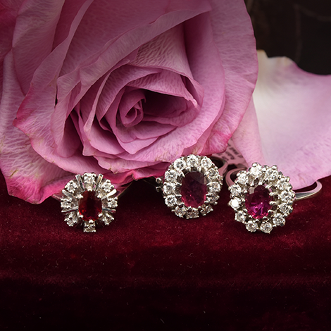 Drei Rubinringe mit Diamanten liegen vor roten Rosen