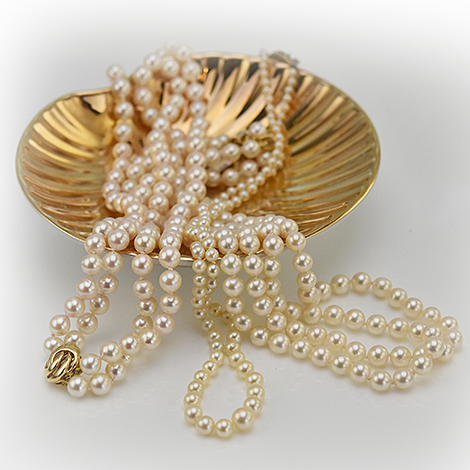 Drei Perlenketten liegen in einer goldenen muschelförmigen Schale
