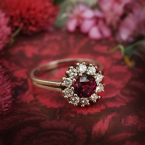 Rubinring mit Diamanten liegt auf floralem, roten Muster
