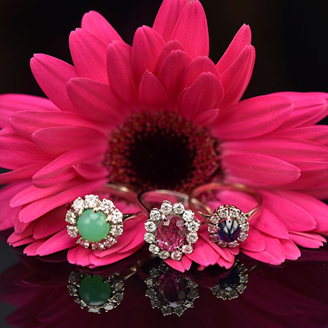 Drei Ringe mit Edelsteinen und Diamanten liegen auf einer pinkfarbenen Blüte 