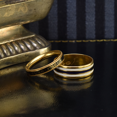 Zwei antike Trauerringe aus Gold und Emaille liegen auf blauem Samt